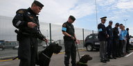 Polizisten mit Hunden stehen vor einem Zaun