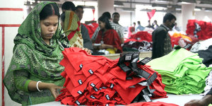 Eine Frau mit halb bedeckten Haaren sortiert rote und grüne Tshirts in einer Fabrik