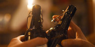 Zwei Bierflaschen werden aneinander gestoßen, dahinter eine Kerze