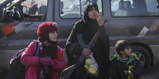 Eine syrische Mutter mit zwei Kindern steht in der Kälte