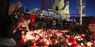 Viele Blumen und Kerzen, daneben sitzen und stehen Menschen