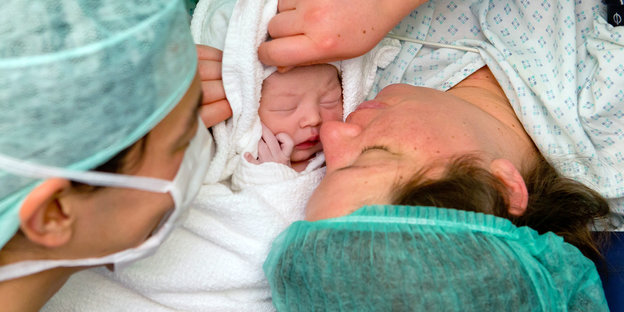 Ein Elternpaar in Klinikkleidung und ein Neugeborenes