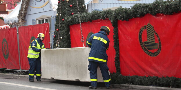 Auf dem Weihnachtsmarkt am Breitscheidplatz installieren zwei Bauarbeiter Betonsperren