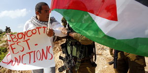 Ein Aktivist hält eine palästinensischen Flagge und ein Schild mit „Boycott, Divestment and Sanctions“ in der Hand