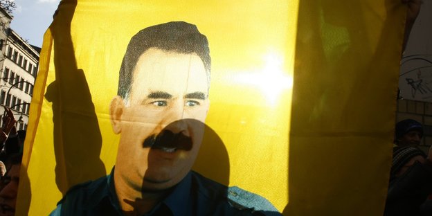 Jemand hält eine Fahne mit dem Porträt von Abdullah Öcalan in die Höhe