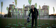 Vor dem Reichstag sind Maispflanzen aus Pappe aufgestellt, ein Aktivist im Anzug hält eine Gießkanne an eine von ihnen