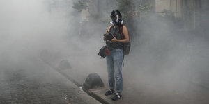 Eine türkische Journalistin steht mit Kamera und Rauchmaske in einer Nebelwolke