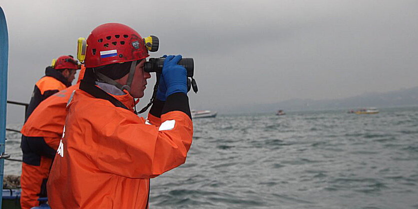 Mann in orangener Kleidung schaut durch Fernglas aufs Meer