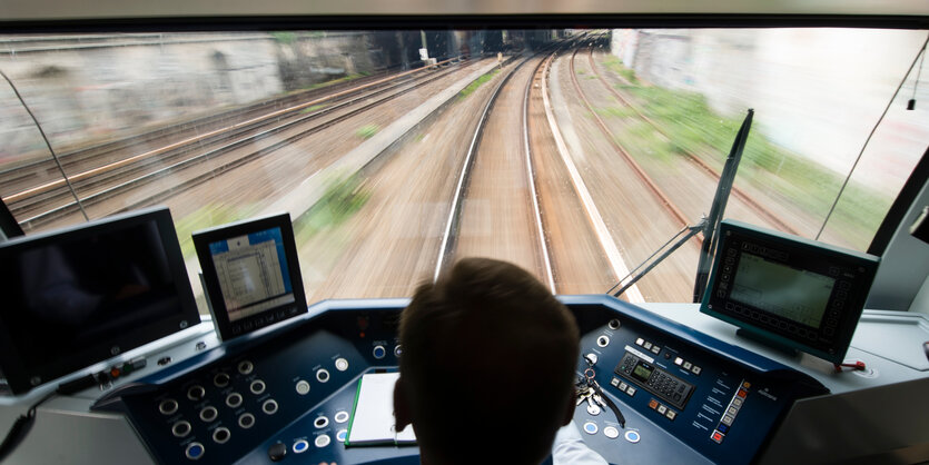 Blick auf den Hinterkopf eines Menschen im Fahrerhäuschen einer S-Bahn und die davorliegende Strecke