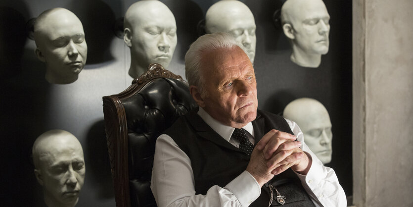 Anthony Hopkins sitzt, in seiner Rolle in "Westworld", nachdenklich vor einer Wand mit weißen Masken