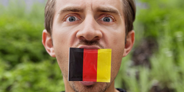 Ein Mann hat eine kleine Deutschlandflagge im offenen Mund