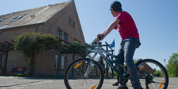 ein syrischer Junge auf einem Fahrrad vor einem verschlossen wirkenden Hof in Mecklenburg-Vorpommern