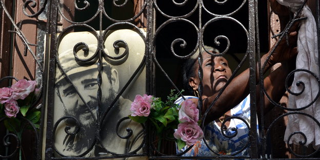 Eine Frau hinter dem Gitter eines Balkons, an das ein Foto von Fidel Castro gelehnt ist