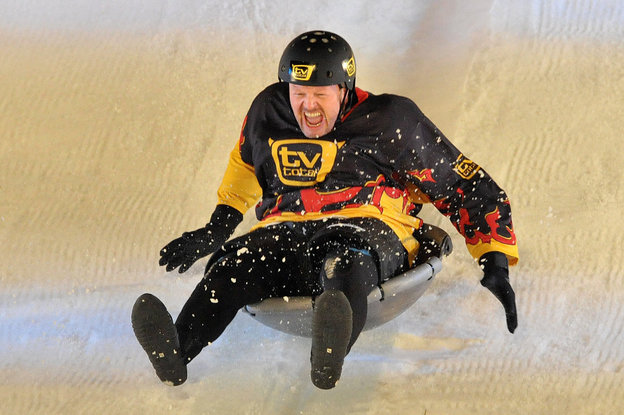 Stefan Raab mit Helm und Deutschland-Outfit rutscht auf einem Schneeflitzer eine Piste runter.