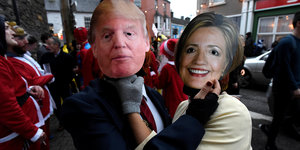 Menschen mit Masken von Trump und Clinton