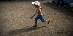 Ein Junge mit einem Cowboyhut läuft über sandigen Boden
