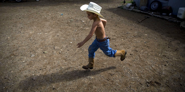 Ein Junge mit einem Cowboyhut läuft über sandigen Boden