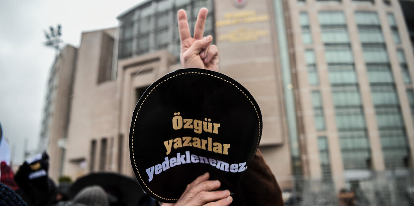 Ein Demonstrant hält ein Schild in die höhe und macht das Victory-Zeichen