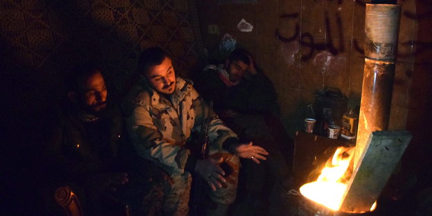 Zwei Soldaten sitzen vor einem Feuer, einer streckt seine Hände in Richtung der Wärmequelle