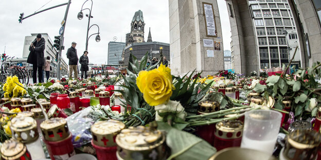 Passanten stehen in Berlin vor einem Blumen- und Kerzenmeer am Breitscheidplatz
