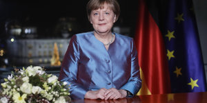 Angela Merkel im blauen Blazer vor Fahnen Deutschlands und der Europäischen Union