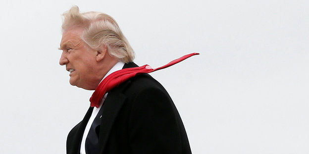 Donald Trump im Gegenwind mit wehendem Haar und fliegender roter Krawatte
