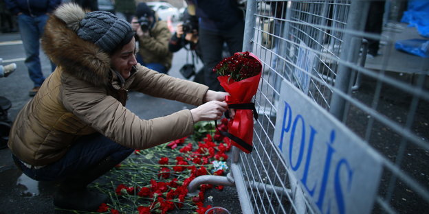Eine Frau legt an einem Absperrzaun rote Blumen nieder