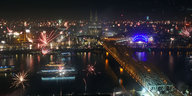 Luftaufnahme des Rheinufers in Köln mit dem Dom bei Nacht, in der Luft ist Feuerwerk