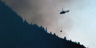 Ein Hubschrauber fliegt über einen Wald und hinein in den Rauch eines Feuers