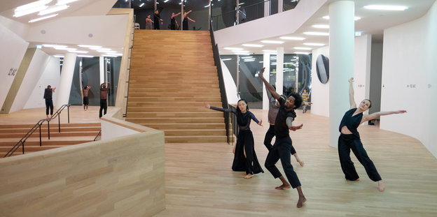 Tänzer in schwarzer Kleidung tanzen in kleineren Gruppen in einem hellen Holzgebäude