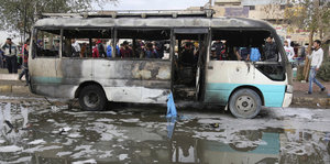 Menschen stehen um einen ausgebrannten Bus