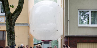 Ein großer weißer Luftballon ist über den Köpfen einiger Menschen eingeklemmt zwischen zwei Hauswänden