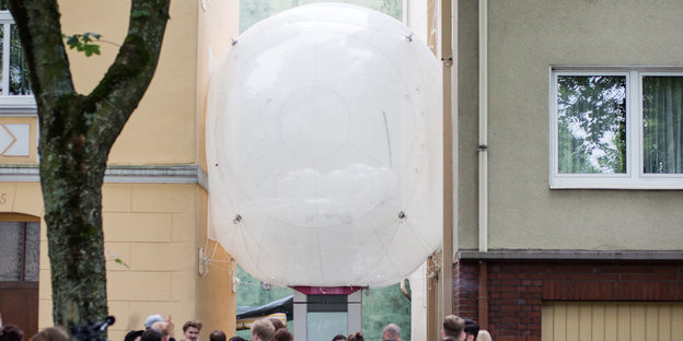 Ein großer weißer Luftballon ist über den Köpfen einiger Menschen eingeklemmt zwischen zwei Hauswänden