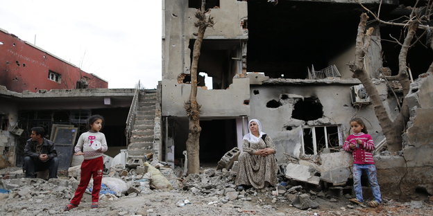 Vier Menschen aus Cizre stehen und sitzen vor ihrem zerstörten Haus