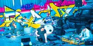 Eine experimentelle Rockband spielt vor einer mit Graffiti bemalten Wand