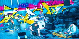 Eine experimentelle Rockband spielt vor einer mit Graffiti bemalten Wand