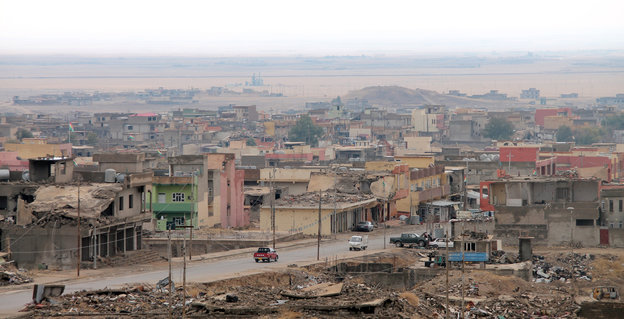 Die verlassene Stadt Sindschar von oben. Viele Gebäude sind zerstört, nur wenige Autos befinden sich auf der Straße. Hinter der Stadt beginnt die Wüste.