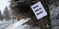 An einem Baum neben einer Straße hängt ein Schild mit der Aufschrift „Horst: Zieh es durch!“