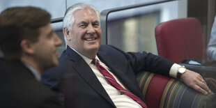 Rex Tillerson sitzt auf einem Sofa und lacht breit