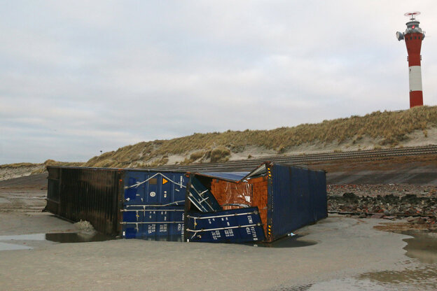 Zwei Container liegen auf dem Strand. Einer davon ist aufgebrochen. Im Hintergrund steht ein Leuchtturm.