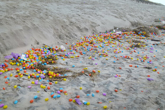 Viele bunte Plastikeier liegen in einer Spur am Strand.