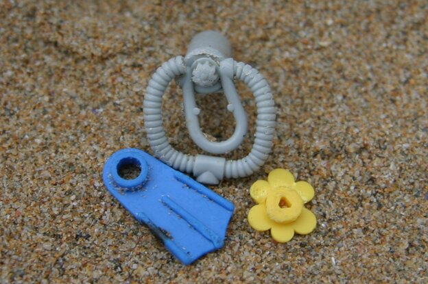 Auf Sand stehen und liegen eine Sauerstoffflasche, eine Flosse und eine Blume. Alles aus Lego.