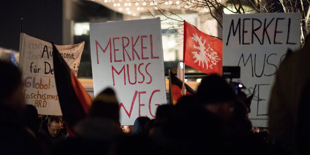 Menschen im Dunkeln. Sie halten Schilder in die Höhe, auf denen steht: „Merkel muss weg"