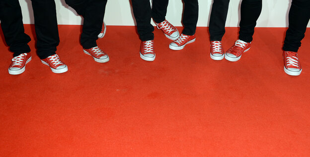 Roter Teppichboden. Darauf mehrere Füße in roten Chucks