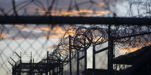 Stacheldrahtzaun rankt sich überall um Guantanamo, dahinter ein rosig-blauer Abendhimmel