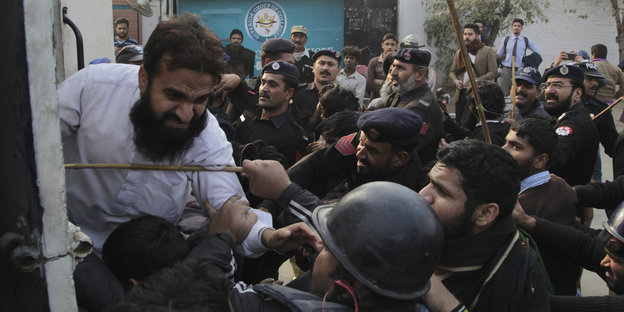 Ein Mann mit verzerrtem Gesicht wehrt sich gegen Polizisten