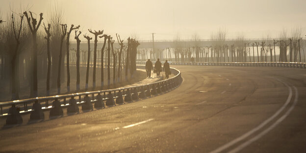 Drei Menschen laufen in der Morgensonne eine Straße entlang