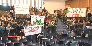 Studenten sitzen und stehen in einem Hörsaal. Sie halten Transparente gegen die geplante Studiengebühr in die Luft.