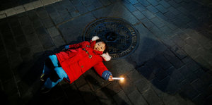 Ein Kind liegt mit einer Kerze in der Hand auf dem Boden