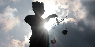 Silhouette einer Justitia-Statue mit Schwert und Waagschalen vor dunklen Wolken